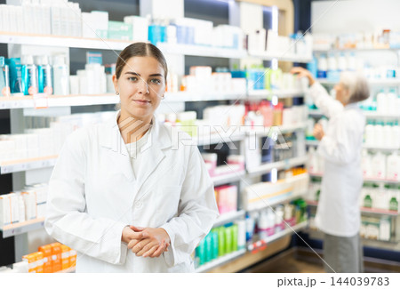 At pharmacy, apothecary waiting for customers and invites with gesture go to department of cosmetics At pharmacy, apothecary waiting for customers and invites with gesture go to department of cosmetics 144039783