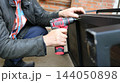 The process of assembling a metal frame. A man in a leather jacket holds a component in place with one hand while carefully driving in a fastener using a compact, red, cordless tool. 144050898
