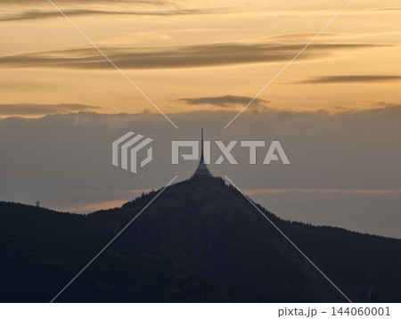 Silhouette of solitary spire over distant hills. Sunset glow illuminating solitary tower on ridge slopes 144060001