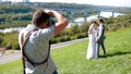 Professional wedding photographer taking pictures of the bride and groom on a hillside covered with green grass 74359567