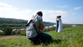 Professional wedding photographer taking pictures of the bride and groom on a hillside covered with green grass 74359569