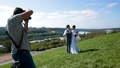 Professional wedding photographer taking pictures of the bride and groom on a hillside covered with green grass 74359571