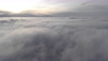 Incredible aerial view shot above swirling fog and clouds at sunset in the mountains. Flying over a low cloud surface with a ridge in the background 77687592
