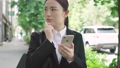 一位身著西裝的年輕女子在城市裡一邊看著她的智能手機一邊環顧四周 83514203