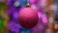 Spinning red Christmas ball on blurry bokeh background of colored and glowing tinsel, holiday lights. Close-up view hanging single festive Xmas ball. Selective, soft focus on foreground. Motion blur 84678054