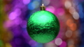 Spinning New Year's ball green color on blurry colored bokeh background of glowing tinsel, holiday lights. Close up of hanging holiday Christmas ball. Soft, selective focus on foreground. Motion blur 84678830