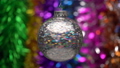 Beautiful multicolored Christmas ball hanging and spinning on blurry colored bokeh background of glowing tinsel, holiday lights. Close up of single holiday toy. Soft and selective focus on foreground. 84678845