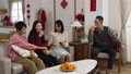 mother giving father cookie while whole family sharing snacks and watching television together in living room on chinese lunar new year. words at background translation: spring and congratulation 84906254
