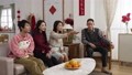 asian family laughing and pointing with finger enjoying watching tv together in living room on chinese lunar new year holiday. word at background translation: spring and congratulation 84906255