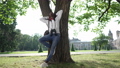 Wide shot relaxed carefree African American young student standing at tree in sunshine outdoors. Portrait of confident happy man leaning on trunk admiring beauty of nature on university yard. 85868318