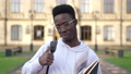 Portrait of happy African American student gesturing thumb up in slow motion smiling looking at camera. Confident smart handsome man in eyeglasses posing at university campus with toothy smile. 85868333