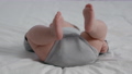 Closeup Of Newborn Baby In Grey Bodysuit Lying On Bed At Home 85881772