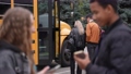 Group of multi-ethnic high school students getting on yellow school bus after lessons, couple of diverse classmates using cellphones while awaiting departure blurred on foreground 86478481