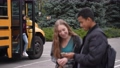 Cheerful caucasian schoolgirl and african american schoolboy enjoying watching social media content on smartphone blurred on foreground while students getting off school bus outside 86478489