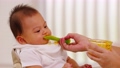 Side view mother feeding her asian baby daughter with pumpkin mashed or vegetable mash on rubber spoon.Mom trying to feed little baby boy at home enjoy and spending time together.Baby feeding Concept 89723844