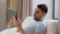 man with tablet computer in bed at home bedroom 90808957