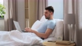 man with laptop in bed at home bedroom 90808965