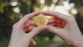 Man shows a cryptocurrency symbol bitcoin coin on the background of a green blurred trees outdoors.  93413209