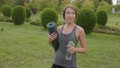 Portrait of a young woman yoga instructor with a fitness mat and a bottle against a green lawn. 93413246