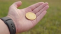 Man shows a cryptocurrency symbol bitcoin coin on the background of a green blurred trees outdoors.  93413317