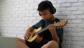 Asian boy learning to play the guitar in virtual meeting for play music online together with friend or teacher in video conference with laptop for online, Communication over Internet Learning concept 94400634