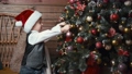 Cute little boy in Santa Claus hat decorating a christmas tree with christmas ornaments baubles 96083234