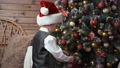 Cute little boy in Santa Claus hat decorating a christmas tree with christmas ornaments baubles 96083235
