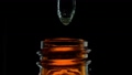Drop of clear liquid, oil, serum or tincture dripping from pipette in the neck of a brown medical bottle. Macro shot of dripping drops of essential oil on black background. 96344544