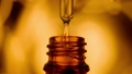 Drop of liquid, oil, medicine or extract dripping from a medical glass pipette in brown bottle. Serum dripping and forming air bubbles in a pipette on blurred yellow background. Concept of medicine. 96344545