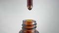 Drop of brown liquid, oil, serum or tincture dripping from pipette in neck of a brown medical bottle. Macro shot of dripping drops of essential oil or iodine on grey background. Aroma, herbal extract. 96344553