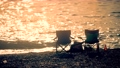 Silhouettes of two empty folding camping chairs set on a pebble beach for romantic picnic at sunset 96628444