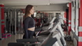 Female athlete in a dark outfit works out on a treadmill in the gym. 100176143