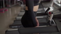 Female athlete in a dark outfit runs on a treadmill in the gym. 100176148