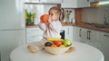 A cute little girl is sitting on the table in front of a plate of fruits and holding an orange in her hands. 100658682