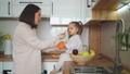 Beautiful mother and daughter spend time together in a white cozy kitchen. Mother feeds her daughter tangerine. Mother's Day 100658687