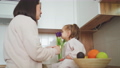 Beautiful mother and daughter spend time together in a white cozy kitchen. The girl is smelling the flowers, and her mother is peeling a tangerine for her. Mother's Day 100658699